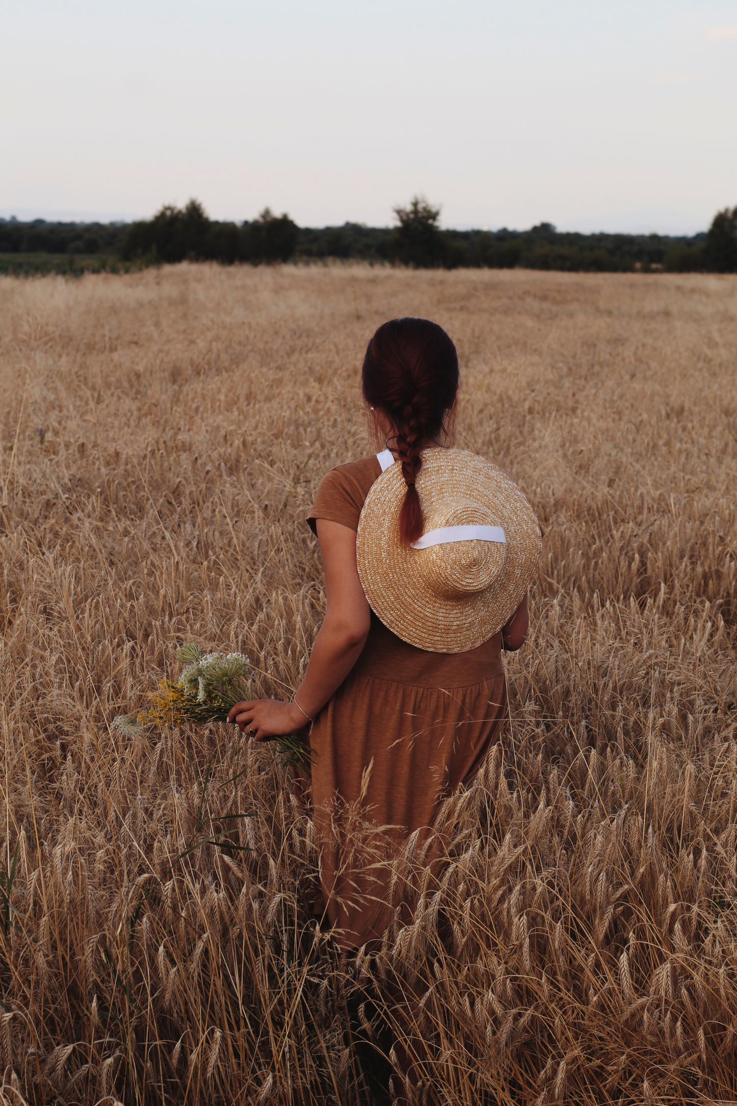 Woman in a brown dress and straw hat standing in a wheat field.