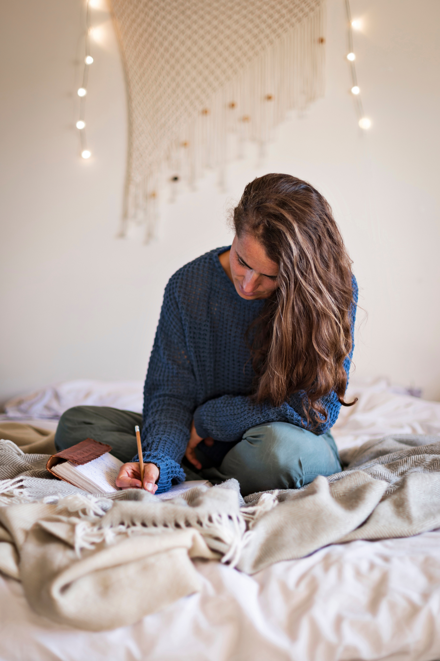 Woman sitting on a bed writing in a notebook with string lights in the background