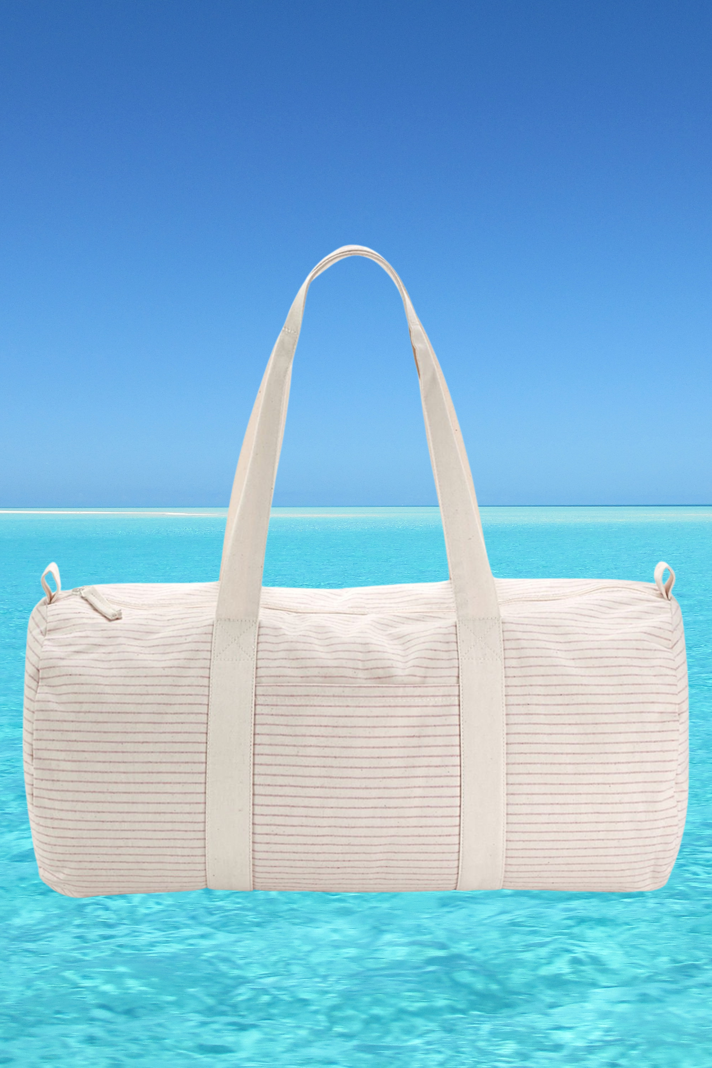 The Meraki Beach CORA organic cotton striped barrel bag in light red with beach back drop