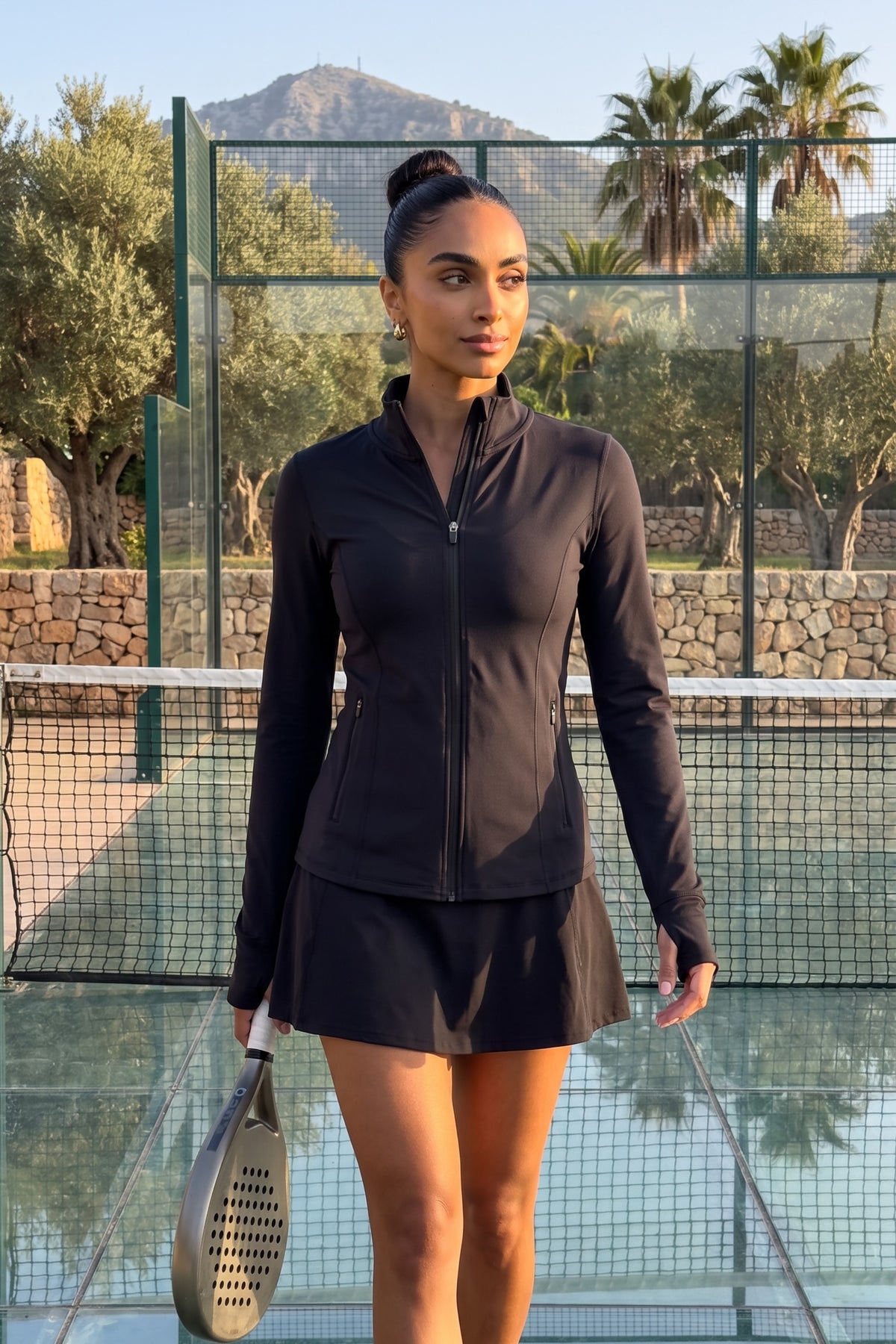 Woman playing padel and wearing the PALMA Women’s Recycled Sports Jacket in Black by Meraki Beach – sustainable high-stretch activewear made from recycled plastic bottles