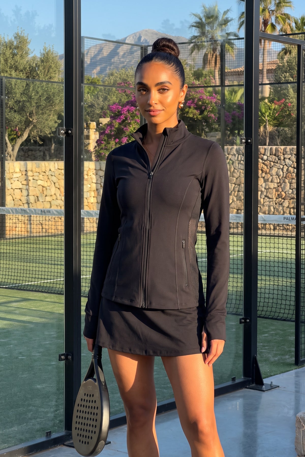 Woman playing padel and wearing the PALMA Women’s Recycled Sports Jacket in Black by Meraki Beach – sustainable high-stretch activewear made from recycled plastic bottles